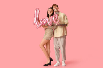 Young couple with air balloon in shape of word LOVE on pink background. Valentine's Day celebration