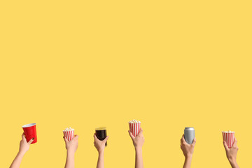Hands holding buckets with popcorn and drinks on yellow background
