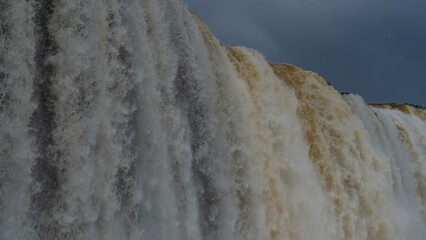 Waterfall streams. Close-up. Powerful jets of foaming white water fall from the edge of the cliff. Texture. Drops, splashes. The blue sky. Iguazu Falls. Brazil.