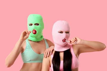 Beautiful young stylish women in balaclavas and sexy underwear with lollipops on pink background