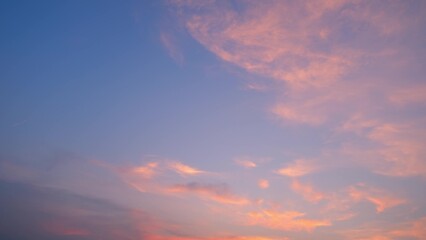A peaceful sunset sky with soft pink and orange clouds scattered across a backdrop of deepening blue. The colors blend harmoniously, creating a serene and calming atmosphere. Sunset sky background.

