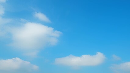A clear blue sky with fluffy white clouds scattered across. The vibrant blue hue and soft clouds create a calming and serene atmosphere, perfect for a sunny day. Wonder of nature background.
