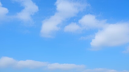 Naklejka premium A clear blue sky with a few scattered, fluffy white clouds. The contrast between the vibrant blue and the soft white clouds creates a serene and peaceful atmosphere. Wonder of nature background. 