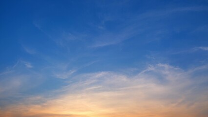 Fototapeta premium A stunning sunset with the sky transitioning from deep blue at the top to warm orange and yellow hues near the horizon. Wispy clouds are scattered throughout, adding texture to the serene scene. 