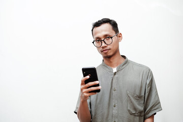 a young man wearing glasses holds a cell phone with a serious expression