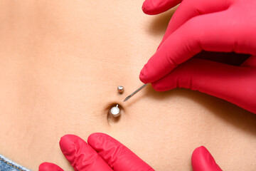 Professional doing piercing of young woman's navel, closeup