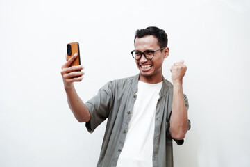A man wearing glasses has a happy expression looking at a cellphone on a plain white background