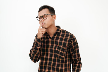 a young man wearing a flannel shirt, wearing glasses is scratching his nose (silly expression) on a plain white background