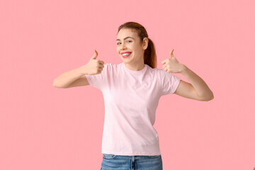 Beautiful young woman with hearing aid showing thumb-up gesture on pink background