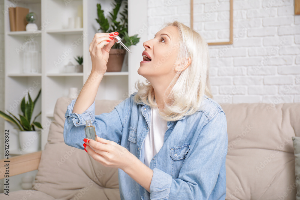 Poster mature woman taking cbd oil on sofa at home