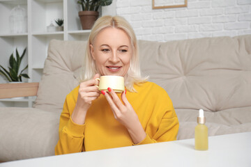Fototapeta premium Mature woman with bottle of CBD oil drinking coffee at home