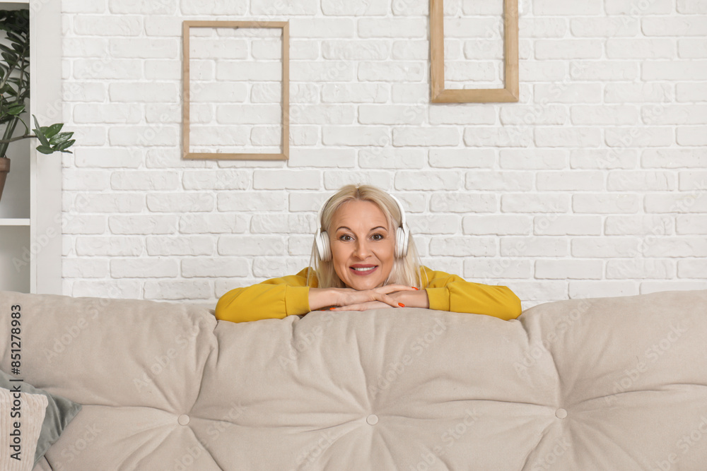 Sticker Mature woman in headphones leaning on sofa at home