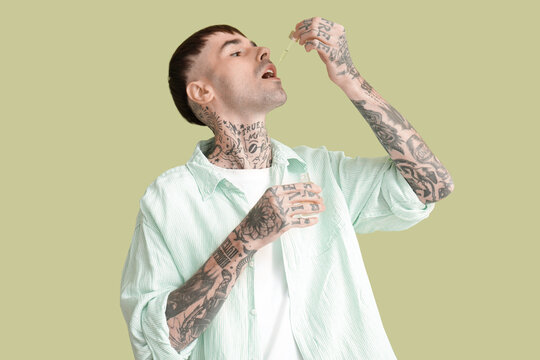 Young tattooed man taking CBD oil on green background