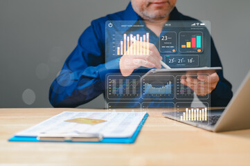 A man is looking at a virtual screen with a lot of graphs and numbers. He is using a tablet to...