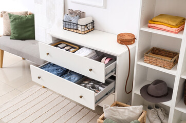Chest of drawers with clean clothes and accessories in room