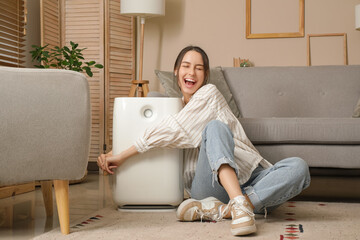 Young woman sitting on floor and hugging modern humidifier in living room