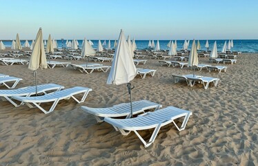 Empty sun beds and umbrellas on sea side. Empty sea beach, no people, end of season,