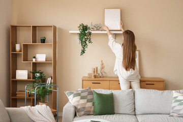 Young woman hanging blank frames on beige wall in modern living room
