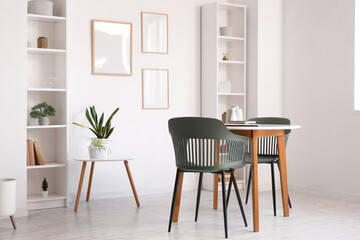 Table with chairs, shelving units and frames on wall in room