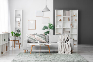 Cozy sofa with plaid and cushions, coffee table, shelving units and frames on wall in living room
