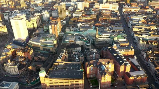 Aerial drone footage of the town centre of Leeds in West Yorkshire UK, showing the whole of the Leeds City Centre and the glass building of the Trinity centre, taken at sunrise with the sun reflecting