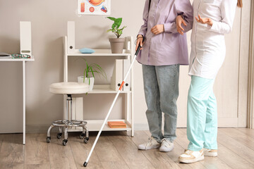 Female ophthalmologist with blind woman walking in clinic