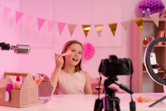 Teenage beauty blogger with makeup brush and powder recording video at table in bedroom