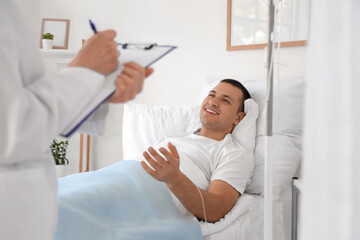 Fototapeta premium Male patient on bed talking to doctor in hospital ward