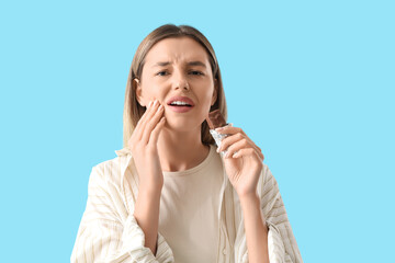 Young woman with sweet candy suffering from tooth ache on blue background