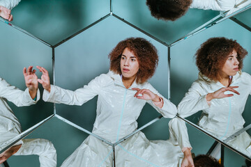 Young woman in white clothes posing in hexagon mirrors in front of grey wall with kaleidoscope effect