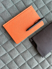 top view of orange notebook with black pen on top, put on a green fabric background