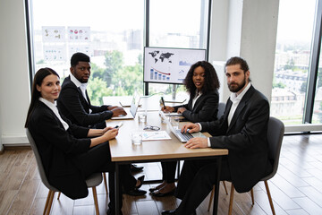 A diverse group of business professionals having a meeting in a modern office, analyzing charts and graphs on a screen.
