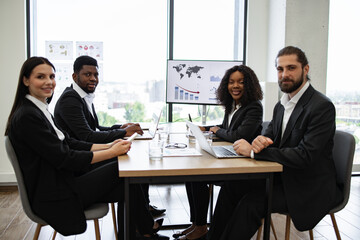 Diverse business team holding a meeting in a modern office, discussing charts and graphs displayed on a screen.
