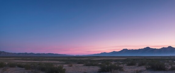 Fototapeta premium A serene panoramic view of a desert landscape at twilight with mountains in the background, perfect for nature-themed uses or contemplative moments.