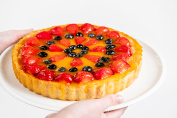 A delicious and mouthwatering strawberry and blueberry cheesecake with mango filling in the hands of a man.