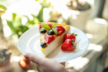 A man's hand holds a plate of appetizing cheesecake with berries. concept of making delicious desserts at home.
