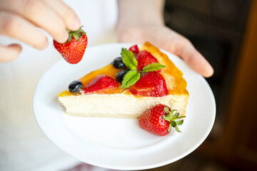 Man holding a plate with appetizing and delicious cheesecake cooked at home. In his hand is a strawberry. The concept of cooking tasty and healthy food.