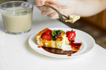 A man sits at a table and eats an appetizing home-made cheesecake with a fork.