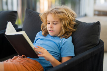 Imagination child. Little child boy lying on the couch at home and reading a childrens story book.