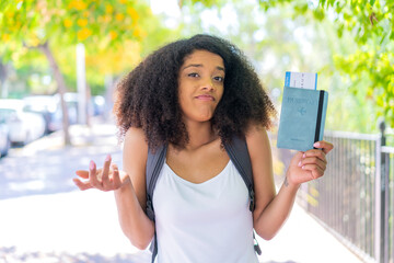 Young African American woman holding a passport at outdoors making doubts gesture while lifting the shoulders