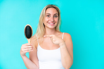 Young caucasian woman with hair comb isolated on blue background and pointing it