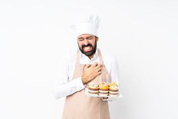 Young man holding muffin cake over isolated white background having a pain in the heart