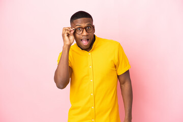 Young latin man isolated on pink background with glasses and surprised