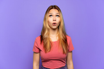 Teenager girl over isolated purple background looking up and with surprised expression