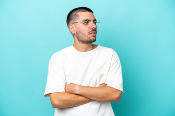 Young caucasian man isolated on blue background looking to the side