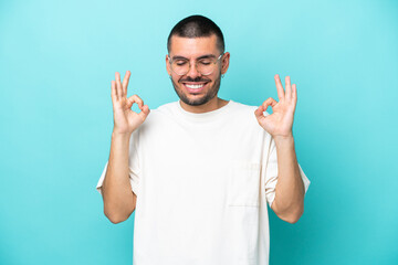 Naklejka premium Young caucasian man isolated on blue background in zen pose