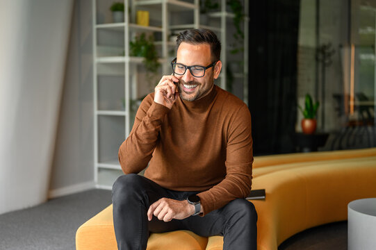 Smiling male engineer discussing project over phone call while sitting on comfortable seat in office