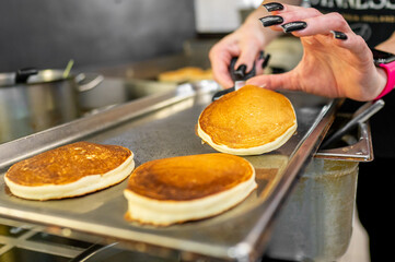 Close-up of hands with black nail polish flipping pancakes on a griddle in a kitchen setting