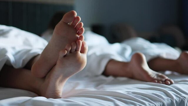 Calm and relaxation on the faces of two kids, whose legs are visible on the large bed of a bright and cozy hotel room. It's a vacation time