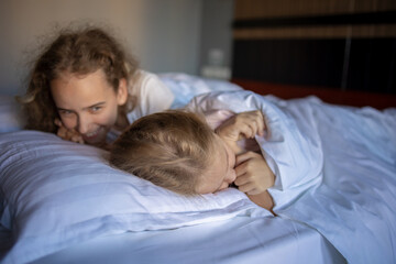 The laughter and joy of two blonde babies playing and fooling around on their big bed after a night...
